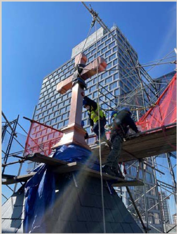 The church's copper cross being hoisted by crane back into place atop the roof
